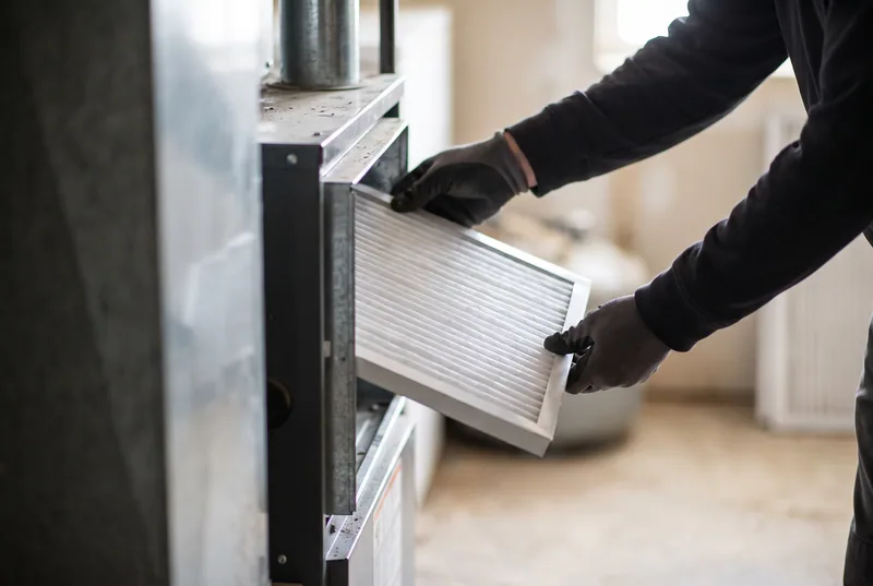 Gloved hands sliding a new pleated filter into a furnace